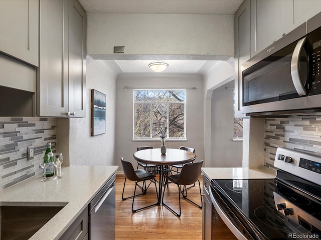 1130 N N Pennsylvania St Unit 306, Denver, CO 80203 - kitchen with stainless steel appliances, backsplash, light stone counters, light wood-type flooring, and a textured wall