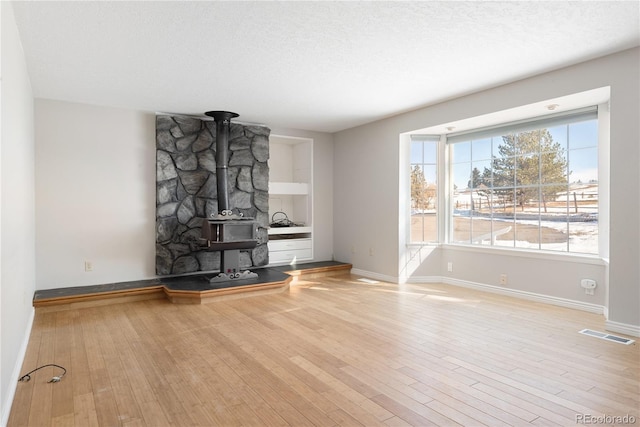 unfurnished living room with a wood stove, built in features, a textured ceiling, and light hardwood / wood-style flooring