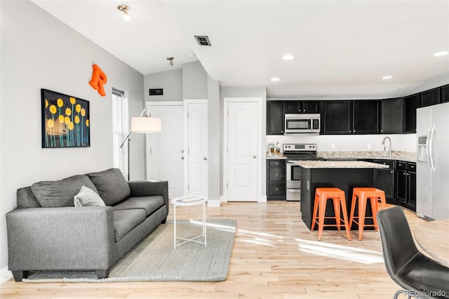 living room featuring light hardwood / wood-style floors, lofted ceiling, and sink