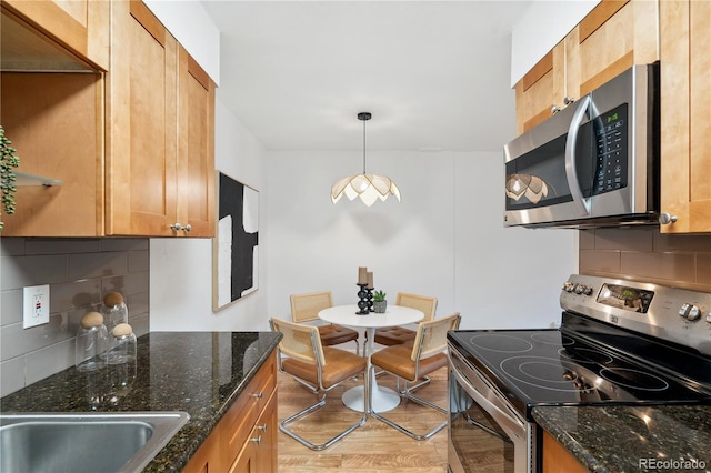 kitchen featuring decorative light fixtures, backsplash, appliances with stainless steel finishes, dark stone countertops, and light wood-type flooring