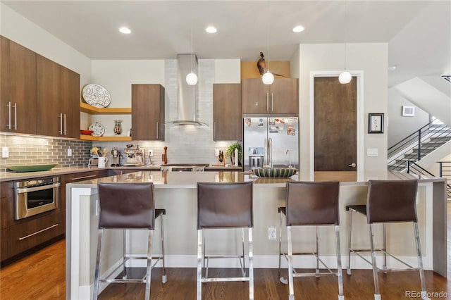 kitchen with stainless steel appliances, hanging light fixtures, wall chimney range hood, and a kitchen bar