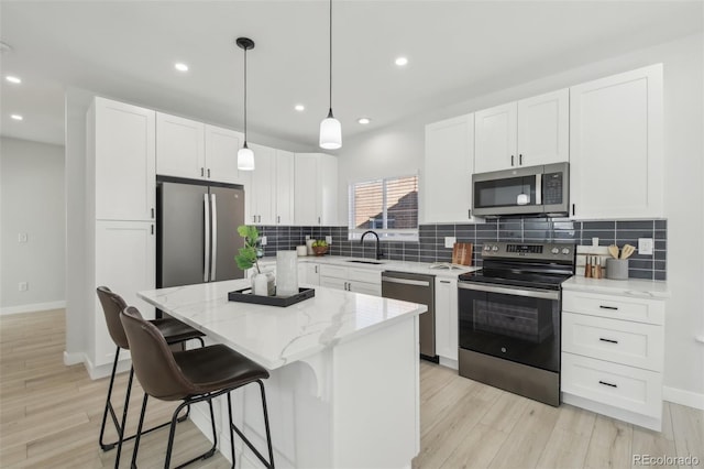 kitchen with a kitchen island, appliances with stainless steel finishes, white cabinetry, hanging light fixtures, and light stone countertops