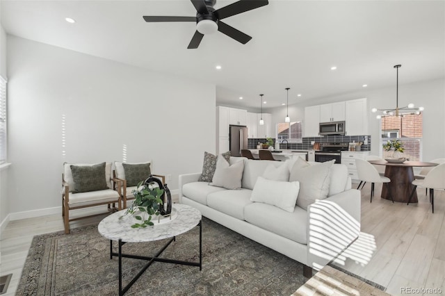 living room with sink, ceiling fan with notable chandelier, and light wood-type flooring