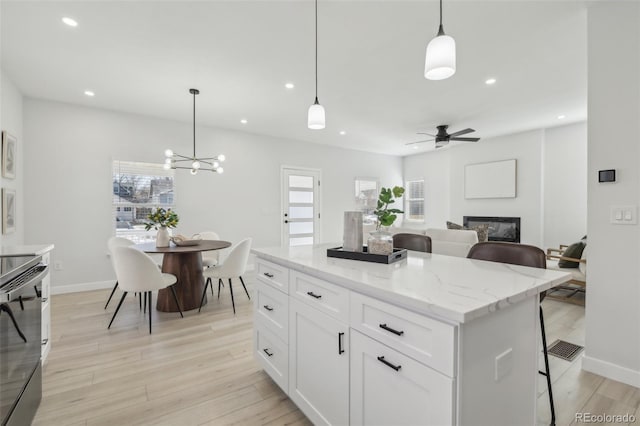 kitchen featuring a breakfast bar area, hanging light fixtures, a center island, light stone countertops, and white cabinets