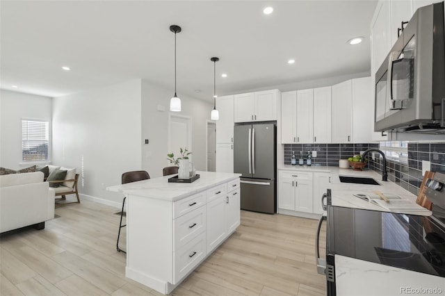 kitchen with sink, white cabinetry, hanging light fixtures, stainless steel appliances, and a kitchen island