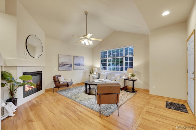 living room with a tile fireplace, lofted ceiling, ceiling fan, and light hardwood / wood-style flooring