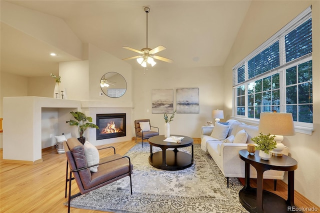 living room with ceiling fan, high vaulted ceiling, a tiled fireplace, and light hardwood / wood-style floors