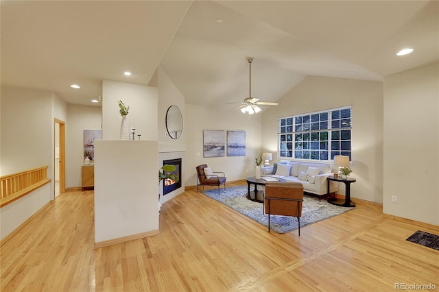 living room with a fireplace, high vaulted ceiling, ceiling fan, and light wood-type flooring