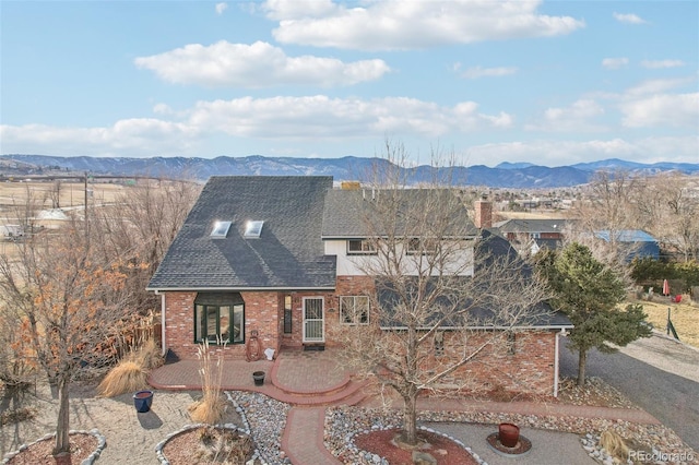 view of front of house with a patio area, roof with shingles, a mountain view, and brick siding