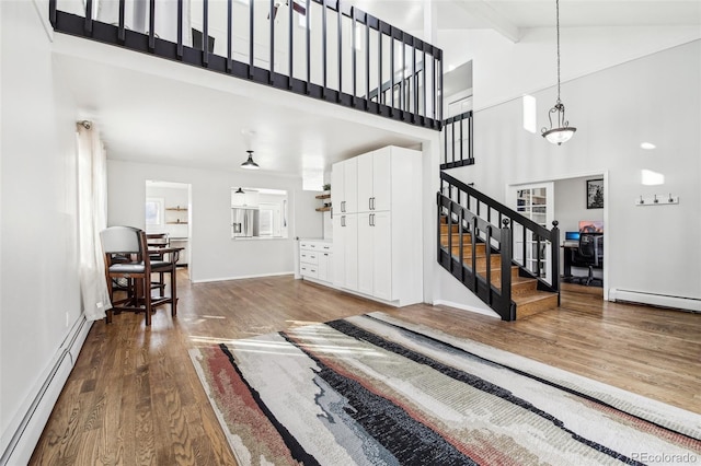 foyer featuring high vaulted ceiling, a baseboard radiator, wood finished floors, stairs, and baseboard heating