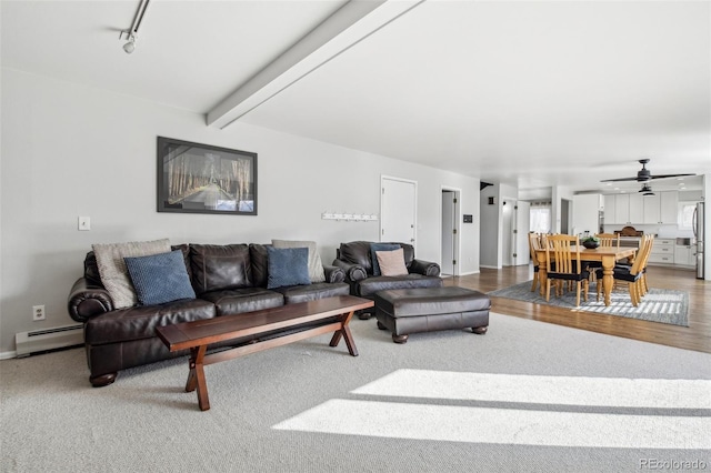 living area featuring beam ceiling, rail lighting, baseboard heating, a ceiling fan, and baseboards