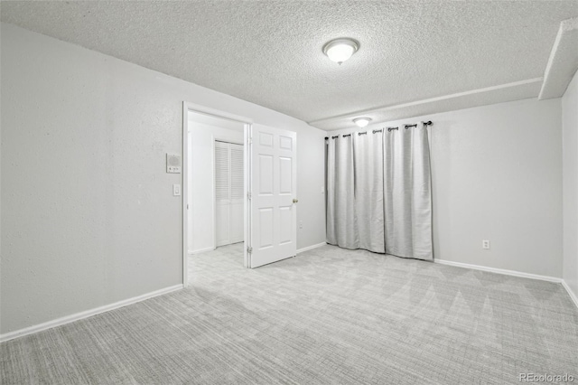 carpeted spare room with a textured wall, a textured ceiling, and baseboards