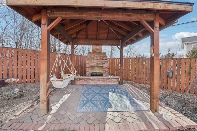 view of patio featuring a gazebo, an outdoor brick fireplace, and a fenced backyard