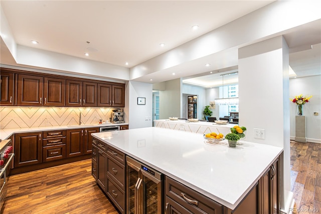 kitchen featuring hardwood / wood-style flooring, beverage cooler, hanging light fixtures, decorative backsplash, and sink