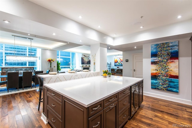 kitchen featuring beverage cooler, hanging light fixtures, dark hardwood / wood-style flooring, a center island, and a breakfast bar area