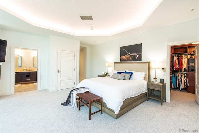 bedroom with a tray ceiling, light colored carpet, a walk in closet, a closet, and ensuite bath