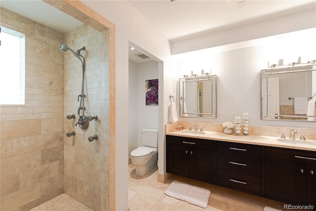 bathroom featuring tiled shower, tile patterned flooring, toilet, and dual bowl vanity