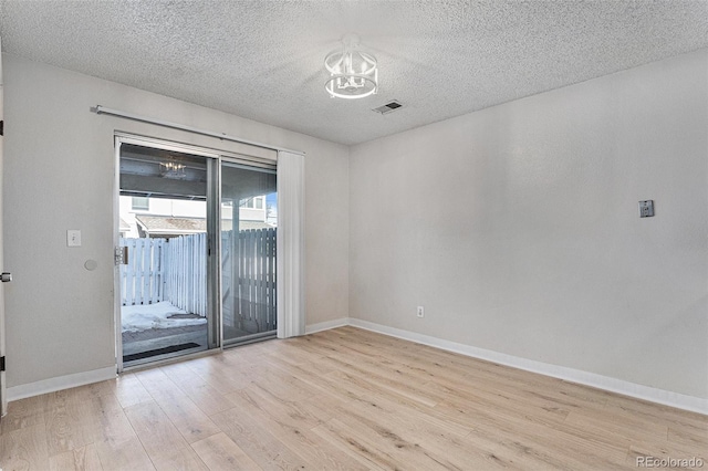 empty room featuring an inviting chandelier, a textured ceiling, and light hardwood / wood-style floors