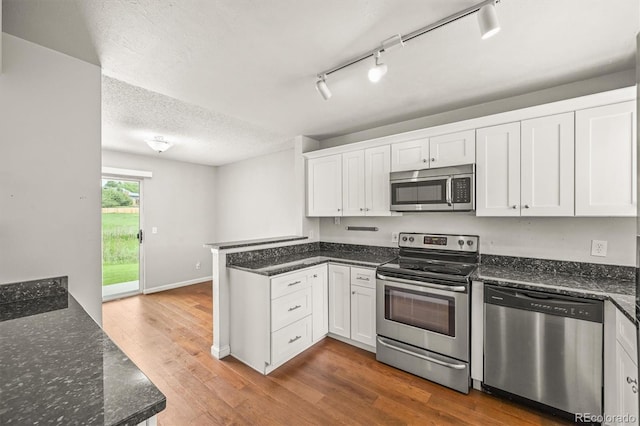 10349 W Fair Ave Unit A, Littleton, CO 80127 - kitchen featuring appliances with stainless steel finishes, a peninsula, white cabinets, wood finished floors, and dark stone counters