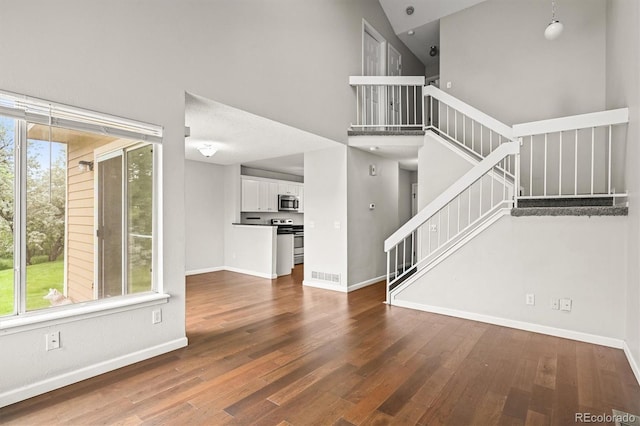 10349 W Fair Ave Unit A, Littleton, CO 80127 - unfurnished living room with baseboards, stairs, wood finished floors, and a towering ceiling