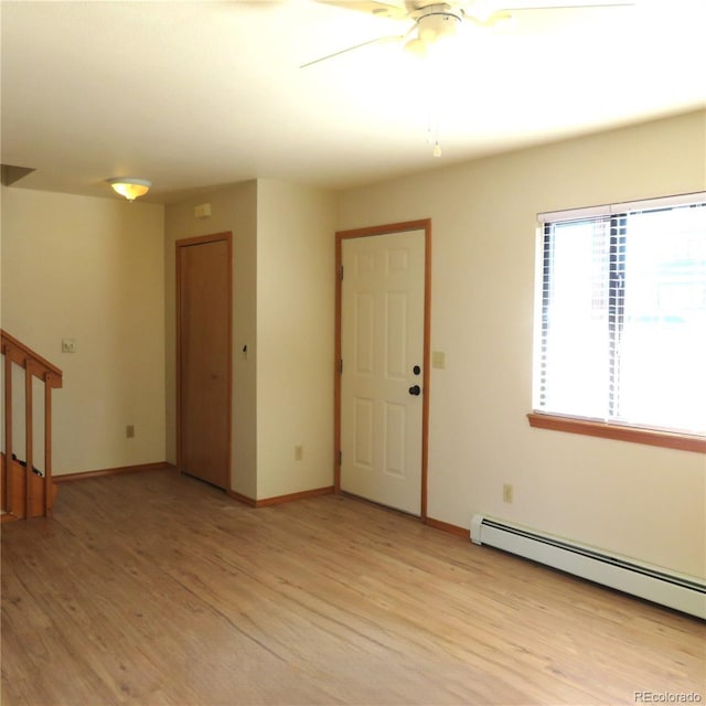 spare room featuring ceiling fan, a baseboard radiator, baseboards, stairs, and light wood-style floors