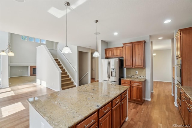 13075 Tamarac St, Thornton, CO 80602 - kitchen with appliances with stainless steel finishes, light wood-style floors, a center island, brown cabinets, and decorative light fixtures