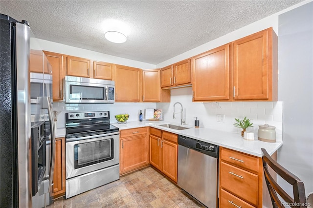 kitchen with a sink, backsplash, stone finish floor, light countertops, and appliances with stainless steel finishes