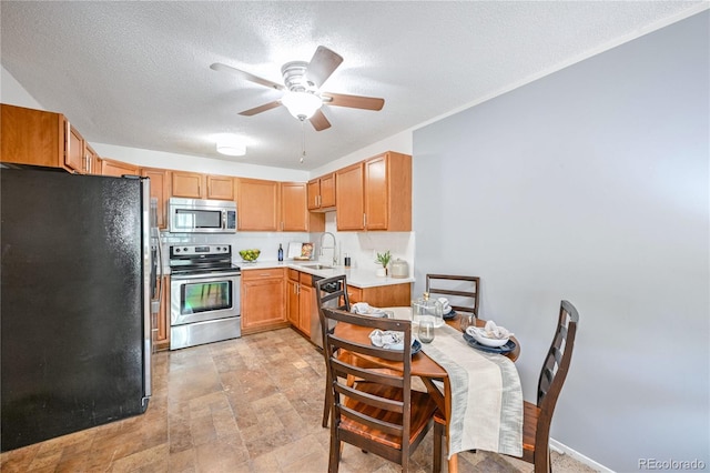 kitchen featuring stainless steel appliances, a sink, a textured ceiling, ceiling fan, and light countertops