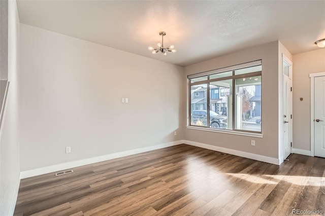 unfurnished room with a notable chandelier and dark wood-type flooring