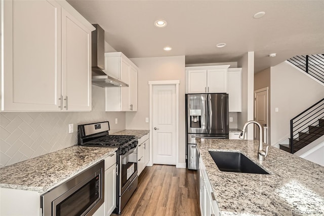 kitchen featuring sink, light stone counters, appliances with stainless steel finishes, wall chimney range hood, and white cabinets