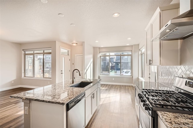 kitchen featuring appliances with stainless steel finishes, a kitchen island with sink, white cabinets, and wall chimney exhaust hood