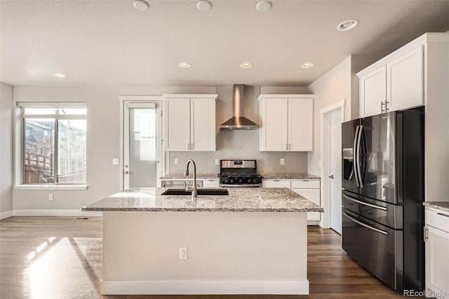 kitchen featuring sink, a kitchen island with sink, gas stove, wall chimney range hood, and fridge with ice dispenser