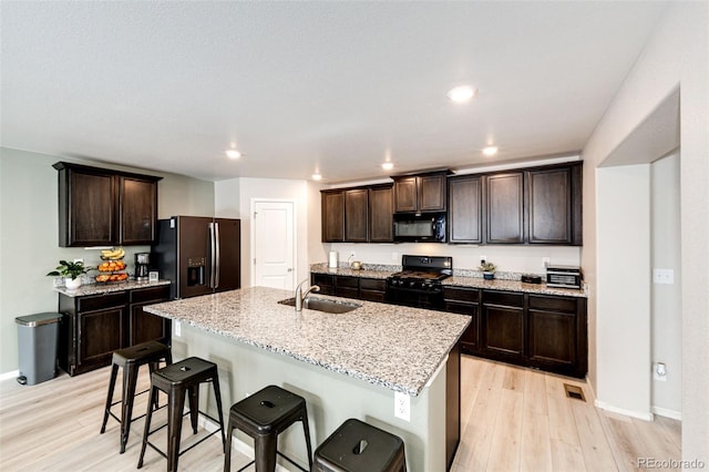 kitchen featuring sink, a kitchen breakfast bar, a kitchen island with sink, dark brown cabinets, and black appliances