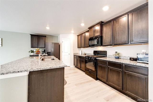 kitchen featuring dark brown cabinets, sink, black appliances, light hardwood / wood-style flooring, and an island with sink