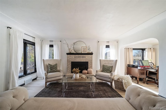 living room with a wealth of natural light, light hardwood / wood-style flooring, and a brick fireplace