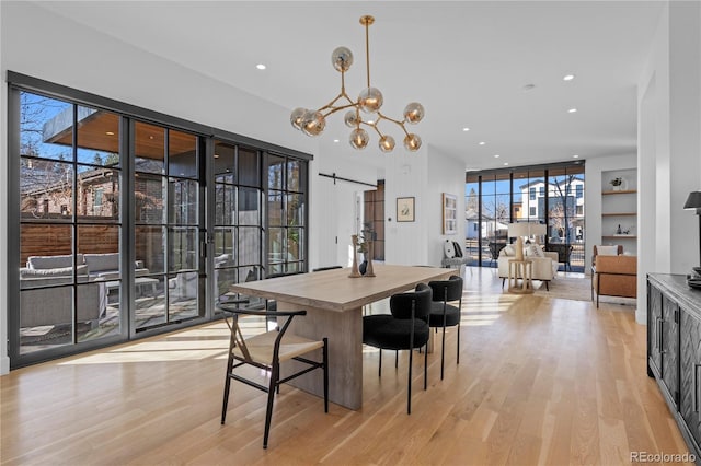 dining area featuring a barn door, light hardwood / wood-style floors, and a notable chandelier