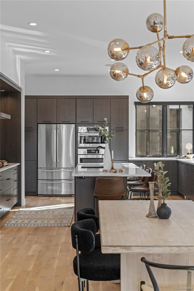 kitchen featuring a kitchen island, appliances with stainless steel finishes, pendant lighting, light hardwood / wood-style floors, and dark brown cabinets