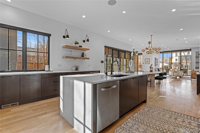 kitchen with an island with sink, dishwasher, sink, dark brown cabinetry, and light hardwood / wood-style flooring