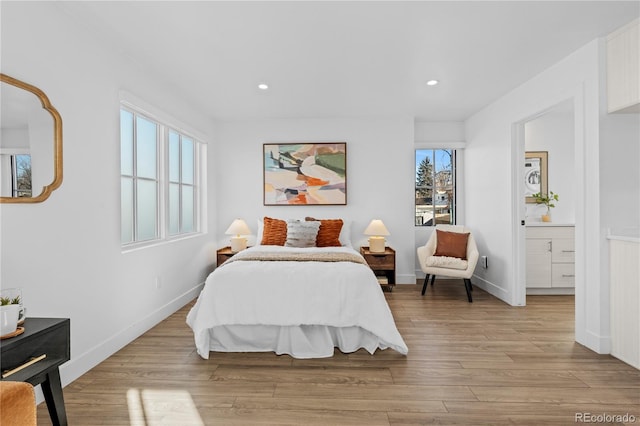 bedroom with multiple windows, ensuite bathroom, and light hardwood / wood-style flooring