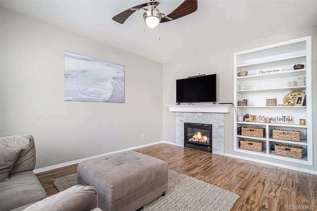 living room with built in shelves, wood-type flooring, and ceiling fan