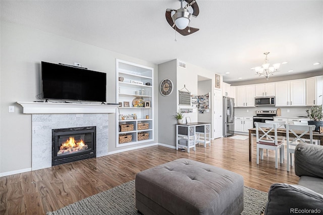 living room with built in features, hardwood / wood-style flooring, ceiling fan with notable chandelier, and a fireplace