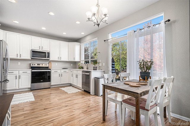 kitchen with appliances with stainless steel finishes, hanging light fixtures, white cabinetry, light hardwood / wood-style floors, and a notable chandelier