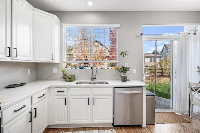 kitchen with white cabinetry, light stone countertops, stainless steel dishwasher, light wood-type flooring, and sink