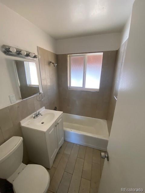 full bathroom with tiled shower / bath, vanity, toilet, and tile walls