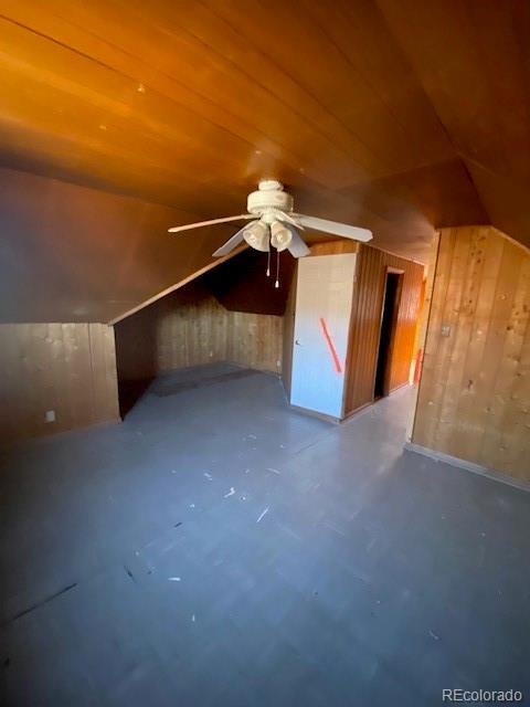 additional living space featuring lofted ceiling, ceiling fan, wooden ceiling, concrete floors, and wood walls