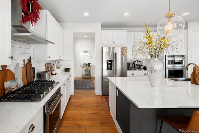 2855 Pawnee Creek Dr, Loveland, CO 80538 - kitchen with stainless steel appliances, wall chimney exhaust hood, wood finished floors, white cabinets, and recessed lighting