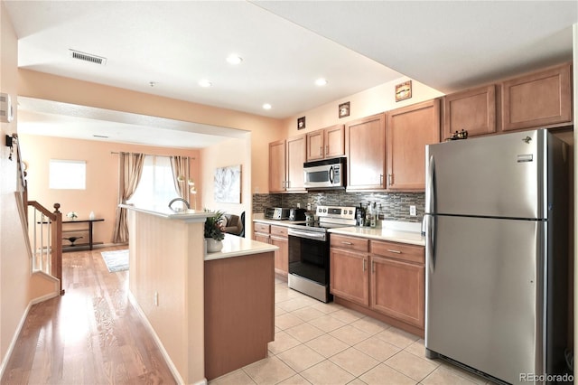 kitchen featuring stainless steel appliances, light countertops, visible vents, backsplash, and a kitchen island