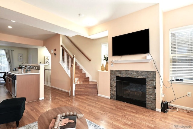 living room featuring baseboards, stairs, a stone fireplace, light wood-type flooring, and recessed lighting