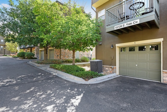 view of side of home featuring driveway, a garage, stone siding, central air condition unit, and stucco siding