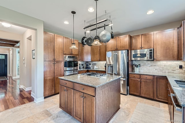 14179 Madison St, Thornton, CO 80602 - kitchen with appliances with stainless steel finishes, light stone counters, tasteful backsplash, a center island, and brown cabinetry